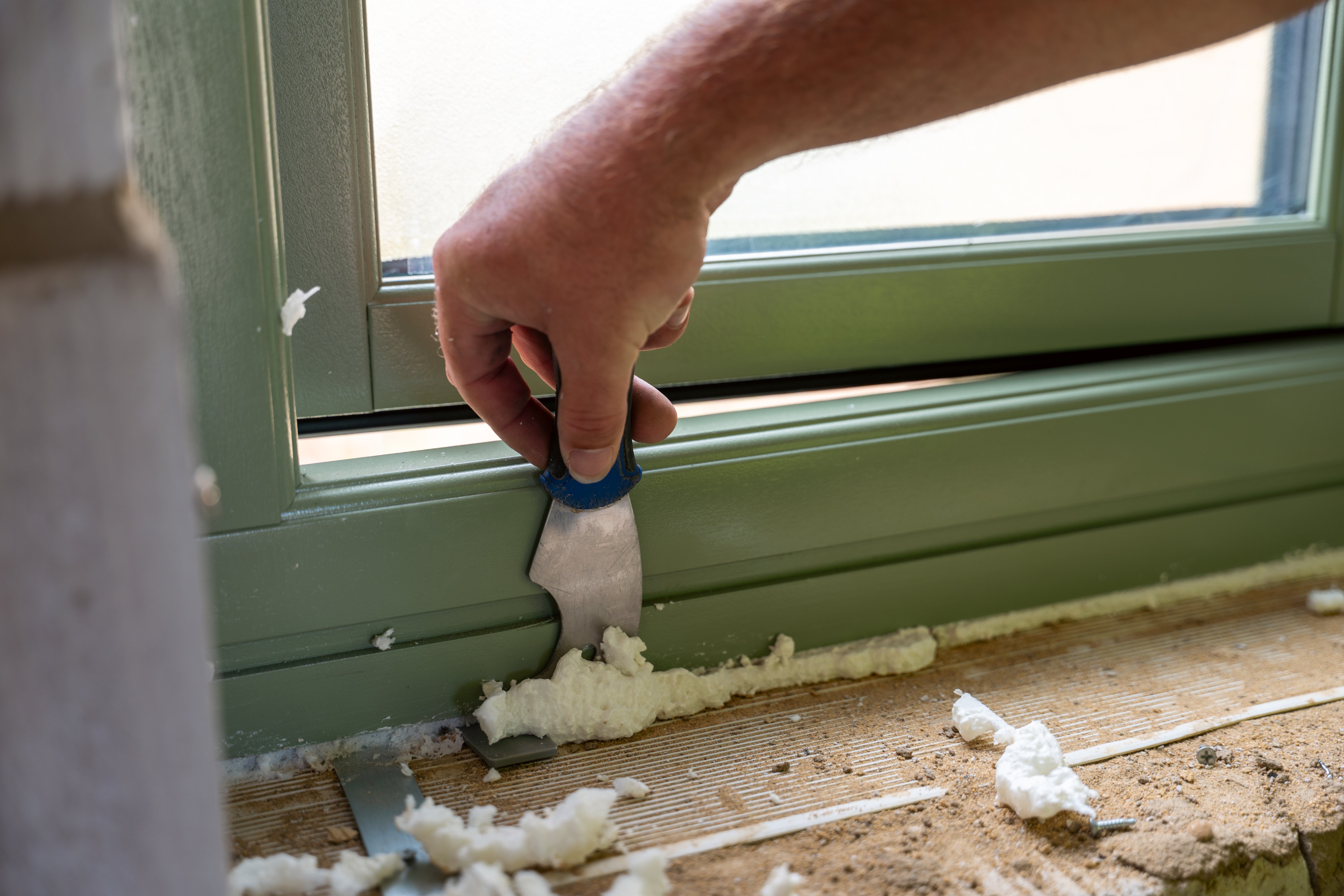 Person applying caulk to a window seal with a caulking gun.